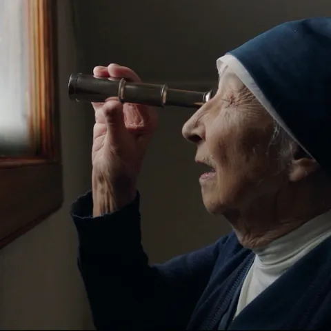 Lady in a nun outfit peeping through a one-eyed telescope.